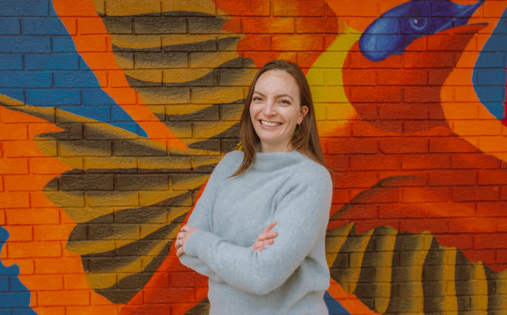 Woman smiling with arms crossed in front of a mural of a bird with outstretched wings