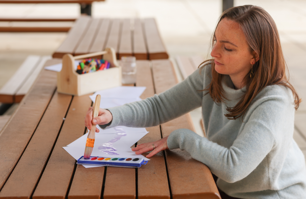 Woman painting on paper with watercolors at a picnic table.